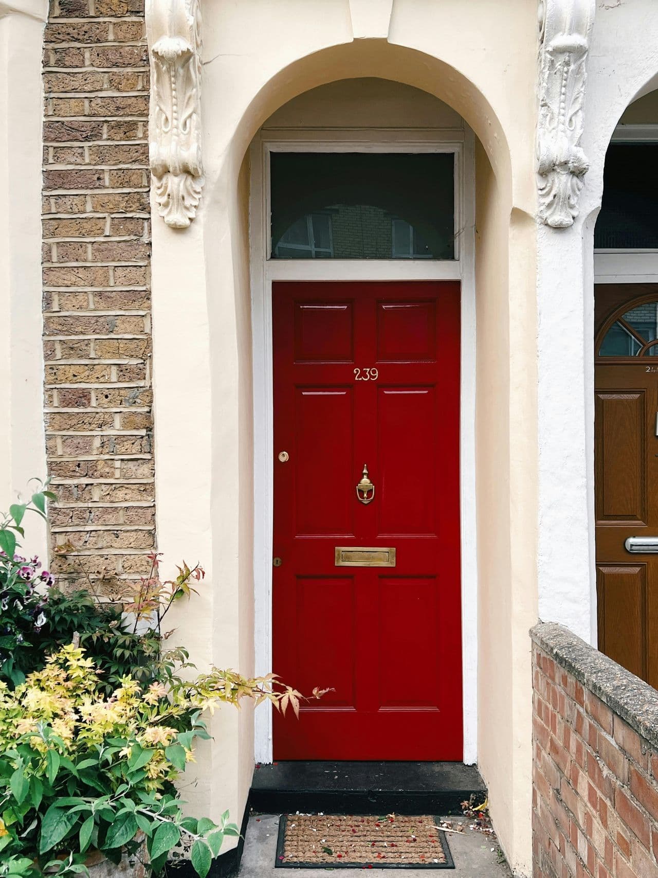 A quaint residential townhouse entrance with a vibrant red door and floral accents